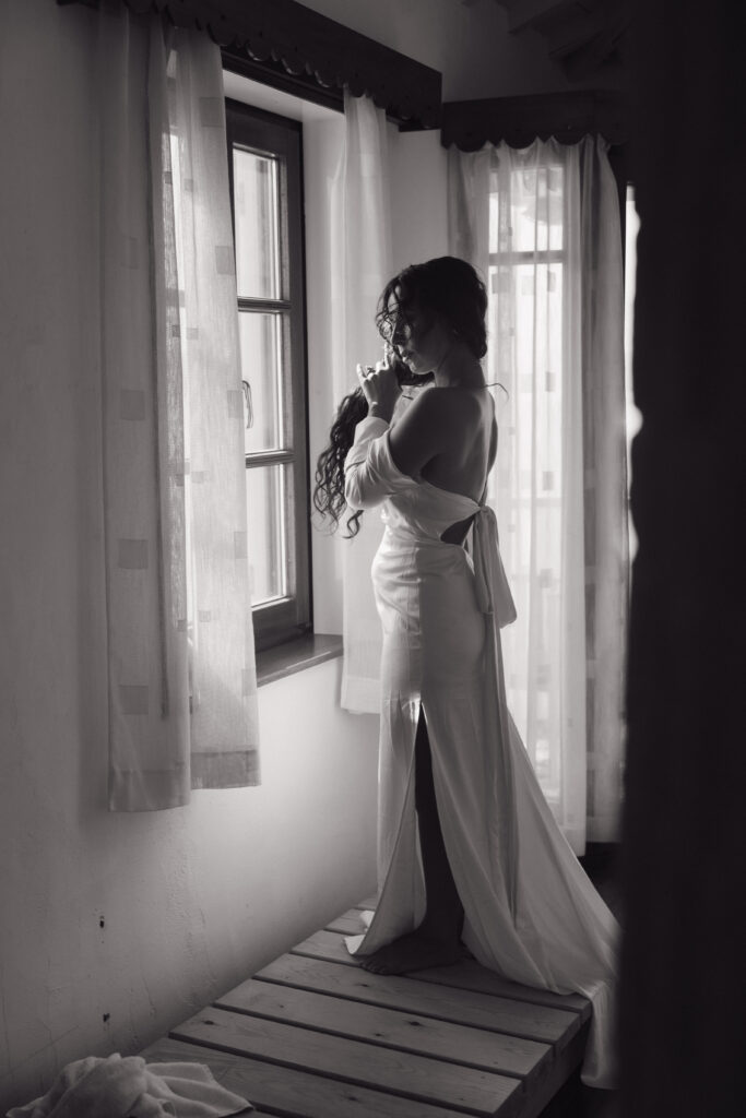 Bride getting ready in their private airbnb in Greece looking out the window at the Aegean Sea before they exchange vows. 