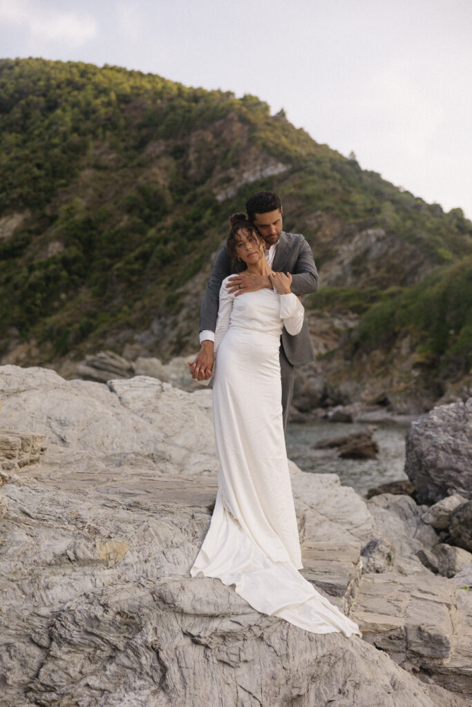 Couple embracing each other on a cliff side in Greece after their intimate elopement overlooking the Aegean Sea. 