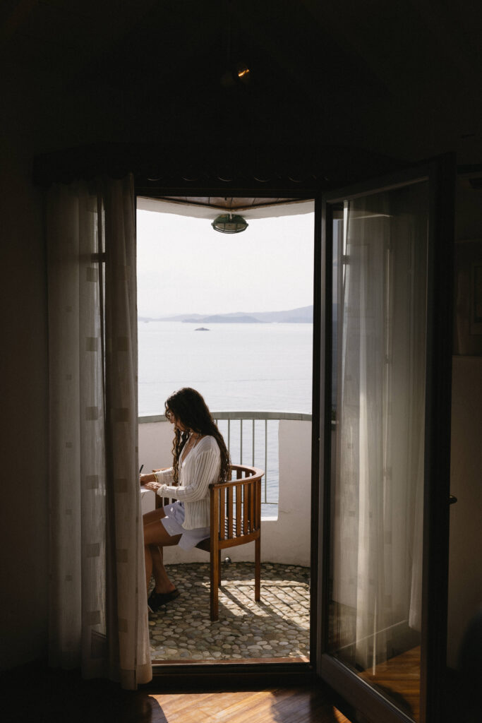 Bride sitting on a balcony overlooking the Aegean Sea in Greece writing her vows to her Fiance before their intimate wedding in Skopelos Greece.